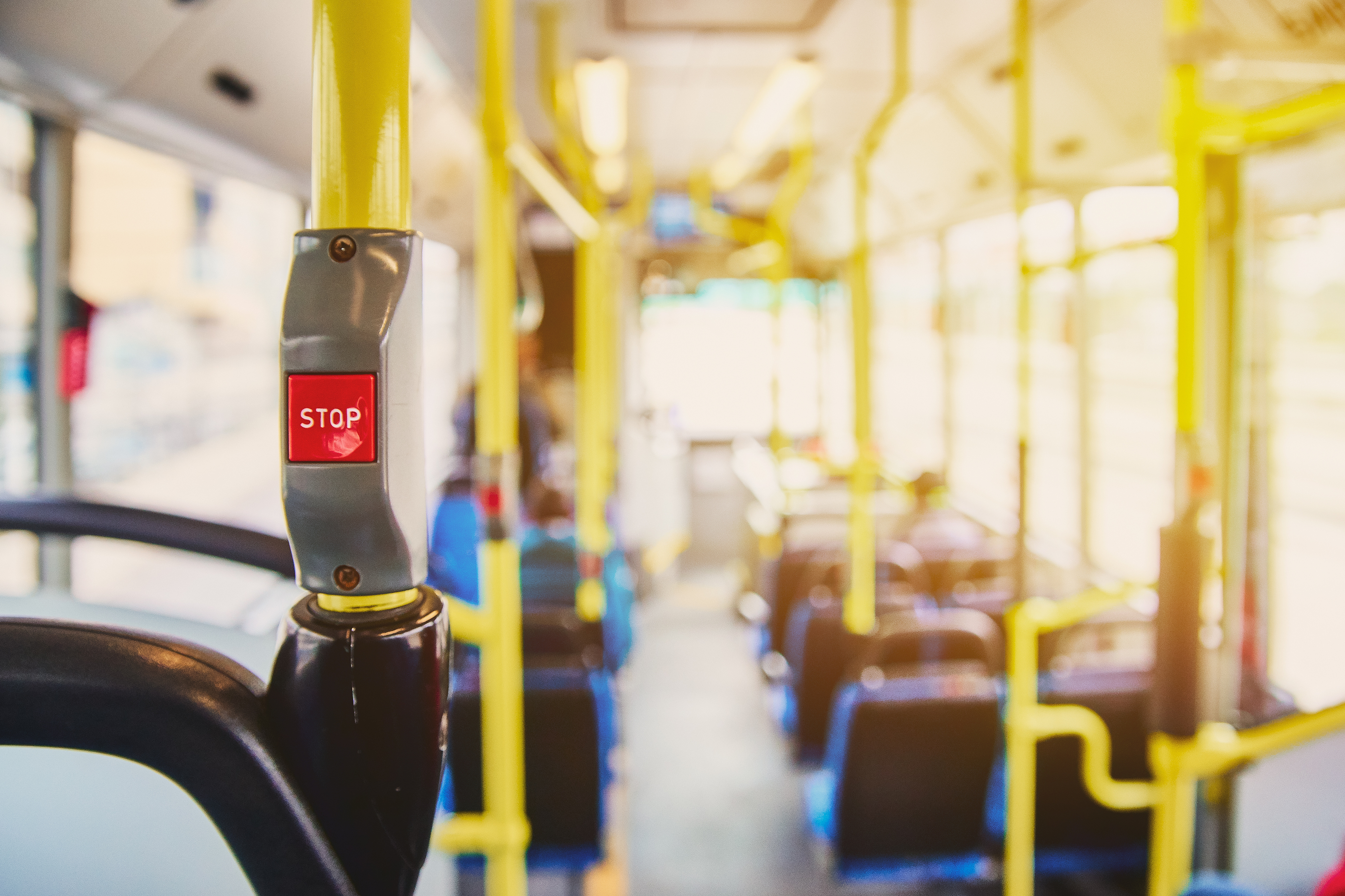 Red button STOP on the bus. Bus with yellow handrails and blue seats. Photo with the sun effect, glare on the lens from the light. Spacious interior of the bus, bright button with focus. Red button STOP on the bus. Bus with yellow handrails and blue seats. Photo with the sun effect, glare on the lens from the light. Spacious interior of the bus, bright button with focus.