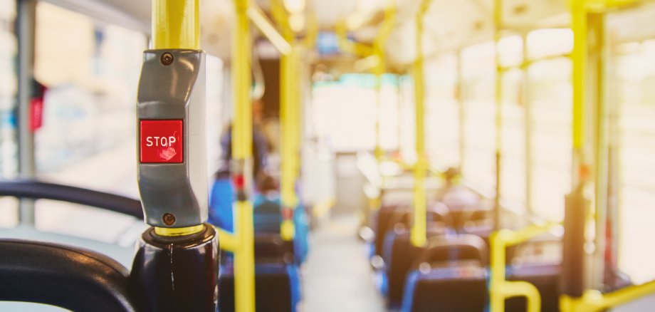 Red button STOP on the bus. Bus with yellow handrails and blue seats. Photo with the sun effect, glare on the lens from the light. Spacious interior of the bus, bright button with focus.