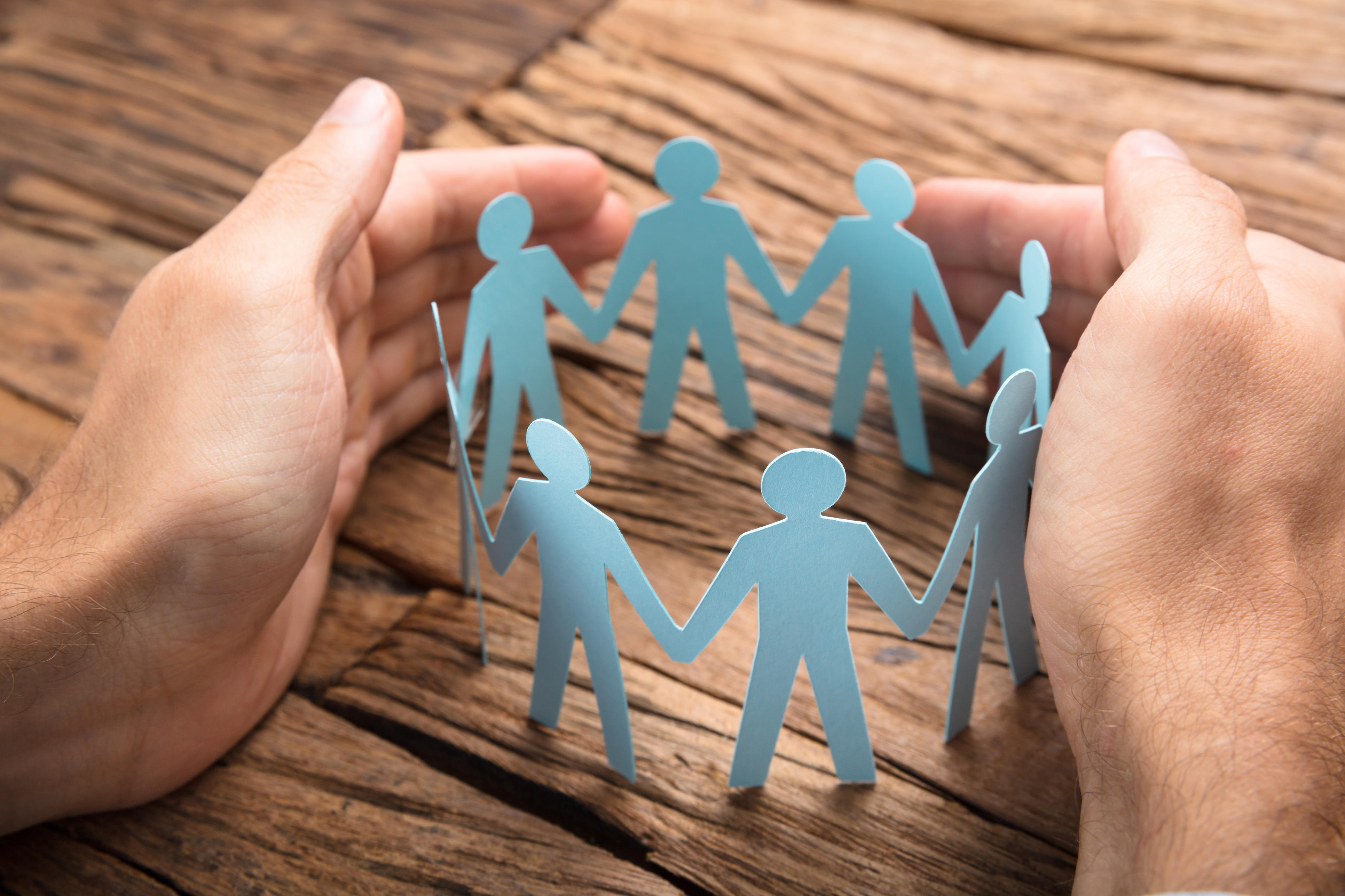 Businessman's Hands Covering Paper Team On Table Businessman's Hands Covering Paper Team On Table