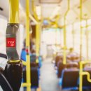 Red button STOP on the bus. Bus with yellow handrails and blue seats. Photo with the sun effect, glare on the lens from the light. Spacious interior of the bus, bright button with focus.