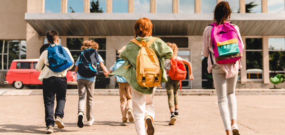 Little kids schoolchildren pupils students running hurrying to the school building for classes lessons from to the school bus. Welcome back to school. The new academic semester year start