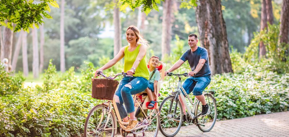 Happy father and mother with kid on bicycles having fun in park.