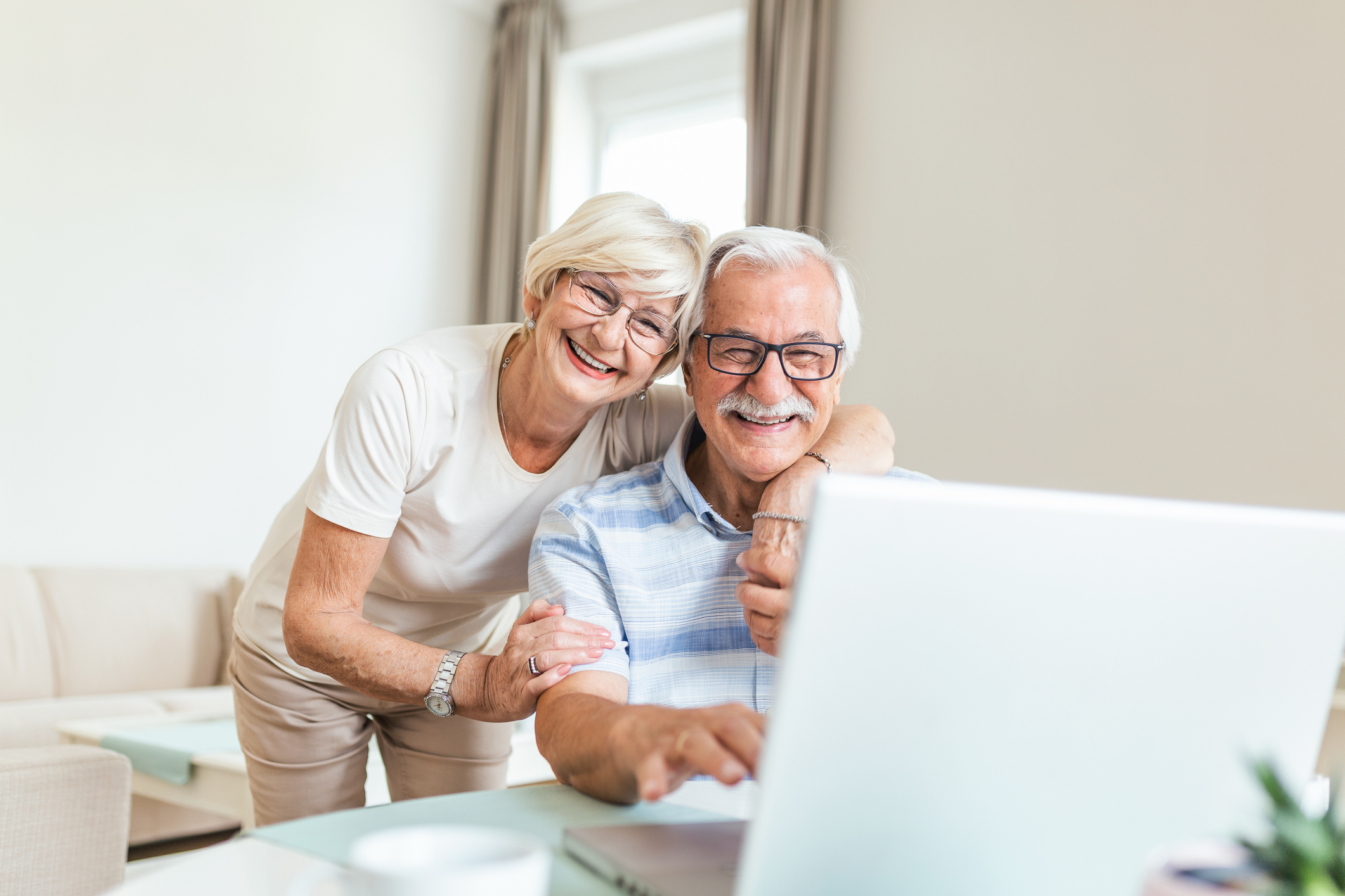 Elderly spouses at home. Wife hugs husband.Having pleasant conversation chatting with grown up children and grandchildren using wireless tech concept Elderly spouses at home. Wife hugs husband.Having pleasant conversation chatting with grown up children and grandchildren using wireless tech concept