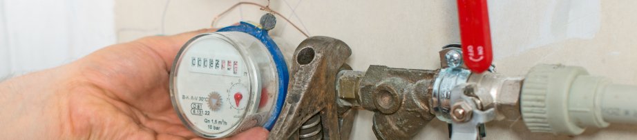 Male plumber fixing water meter with adjustable wrench.