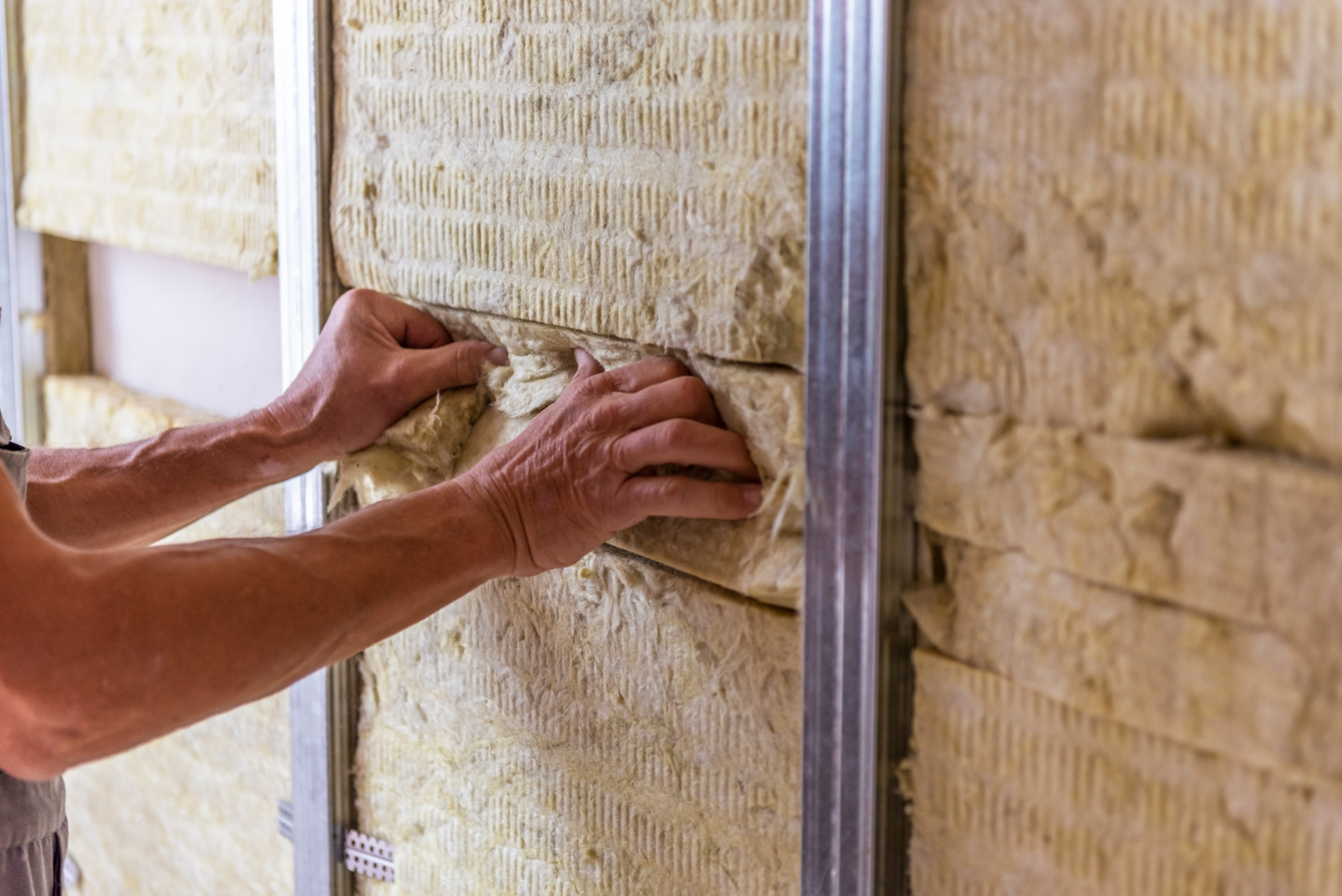 Worker insulating a room wall with mineral rock wool thermal insulation. Worker insulating a room wall with mineral rock wool thermal insulation.