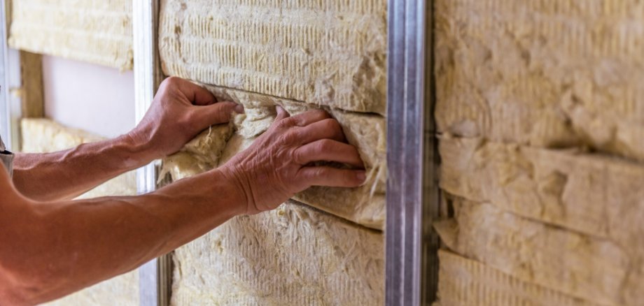 Worker insulating a room wall with mineral rock wool thermal insulation.