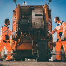 Two refuse collection workers loading garbage into waste truck