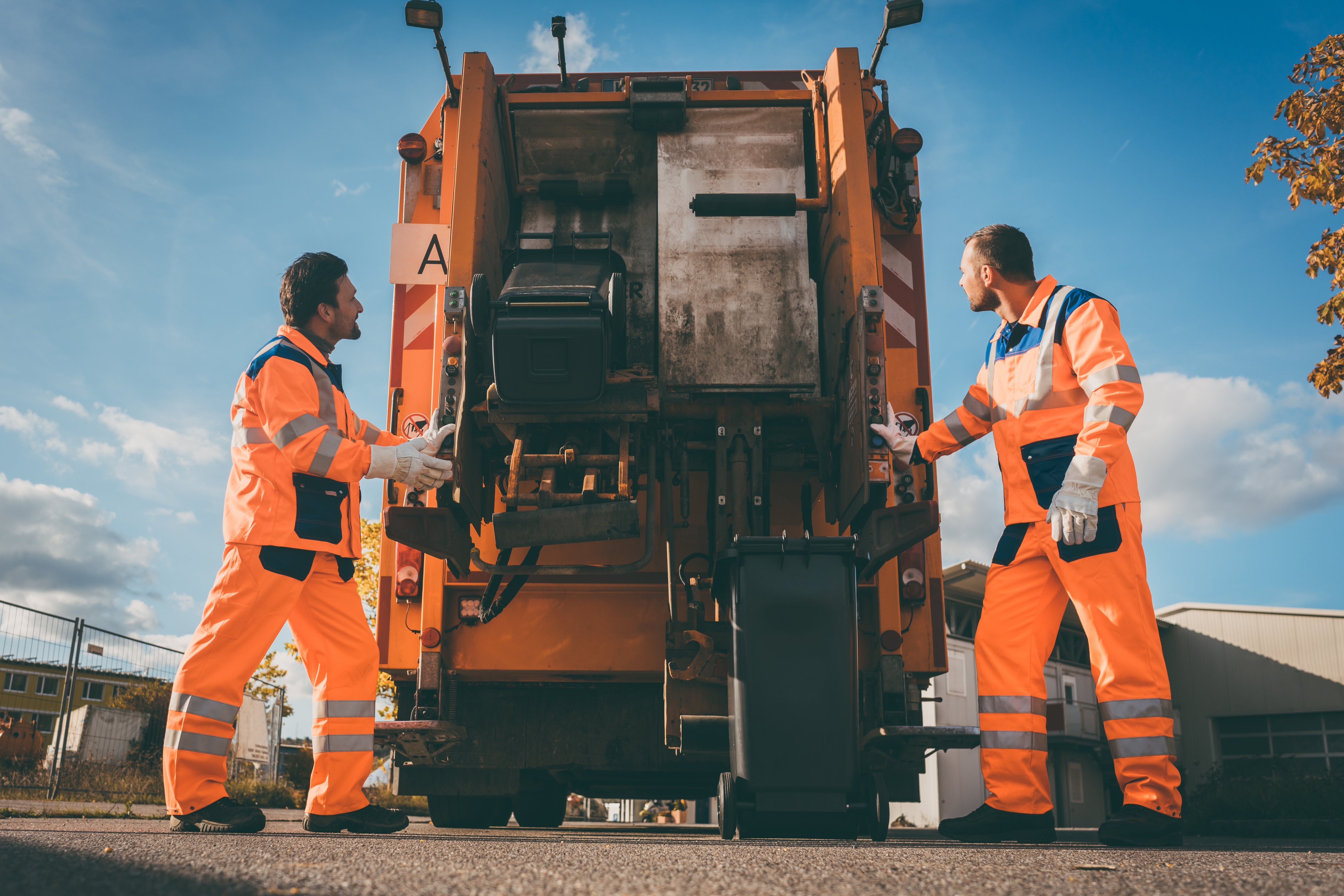 Two refuse collection workers loading garbage into waste truck Two refuse collection workers loading garbage into waste truck