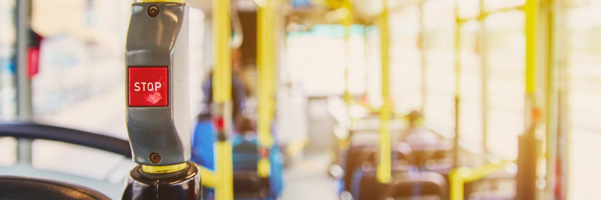 Red button STOP on the bus. Bus with yellow handrails and blue seats. Photo with the sun effect, glare on the lens from the light. Spacious interior of the bus, bright button with focus.