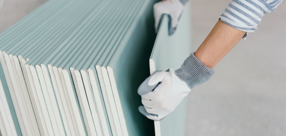 Person wearing gloves taking a sheet of chip board